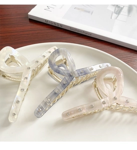 Detail of three acetate shark hair clips in white, blue, and pink with rhinestone decor