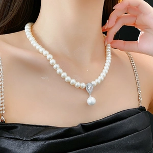 Macro detail of pearl necklace featuring a zircon teardrop pendant on a model neckline