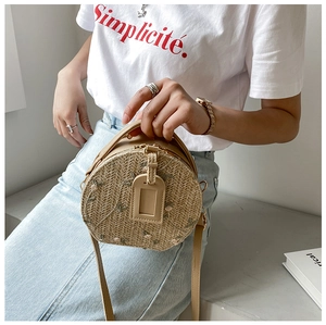 Detail of round straw bag featuring floral embroidery and pearl accents with metallic zip