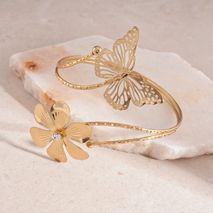 Dettaglio di farfalla dorata e fiore di strass su un bracciale rigido aperto goffrato