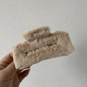 Detail of a large rectangular khaki faux fur hair claw clip held in hand for hair styling