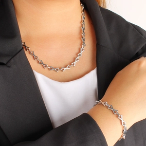 Parure de collier et bracelet argentés à maillons en X portés par une femme