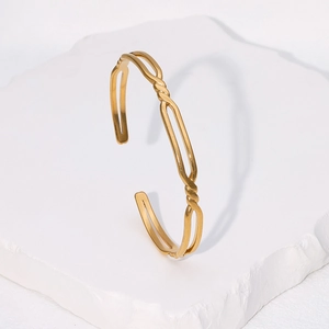 Bracelet jonc ouvert torsadé en acier inoxydable doré posé sur une pierre blanche