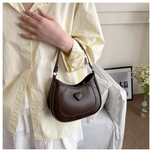 Close-up of a brown leather crescent shoulder bag with embossed heart detail on a model