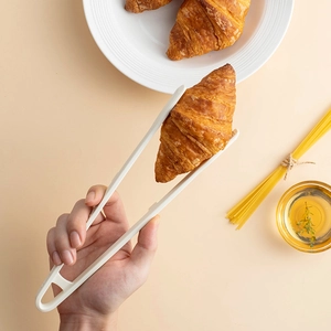 Silicone food tongs in white picking up a croissant on a stylish kitchen table setting