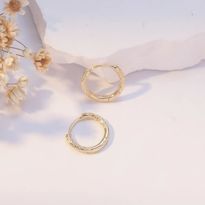 Vintage golden hoop earrings with embossed floral patterns on white stone background