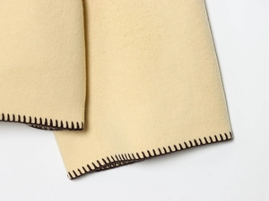 Detail of beige knit sweater with dark brown blanket stitch edging on a white background