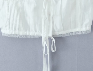 Detail of white cropped top featuring delicate lace trim and pleated texture with tie-front