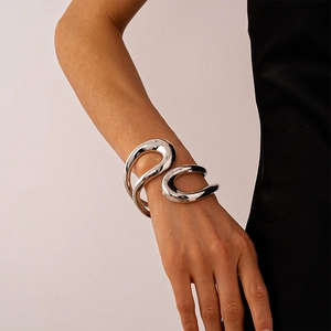 Dettaglio del bracciale rigido aperto scultoreo in argento indossato su tessuto nero