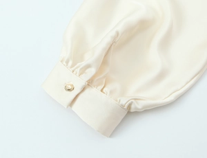 Detailed macro view of cream satin sleeve with elegant gold button and pleated cuff