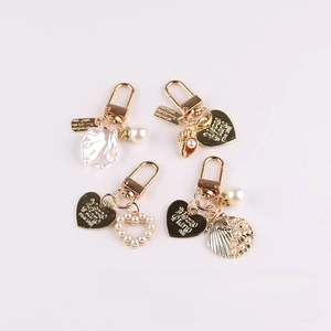 Set of gold keychains with glass pearls and engraved shell pendants on white background