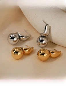 Detailed close-up of polished gold and silver spherical earrings on minimalist pedestals