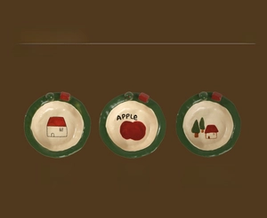 Detailed view of hand-painted ceramic bowls featuring house and apple patterns with green wavy edges