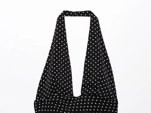 Detail of black halter neck dress with white polka dot pattern and deep V-neckline