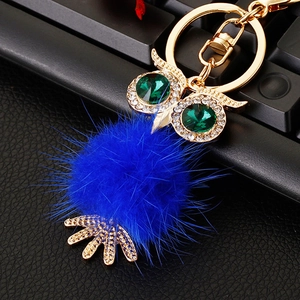 Macro view of crystal owl keychain with blue faux fur pompom and green gemstone eyes