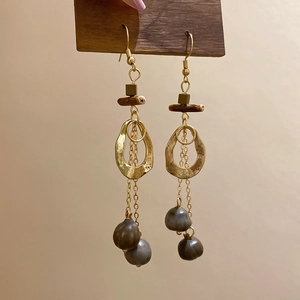 Detail of bohemian wood earrings with gold rings and long tassel chains on a beige wall
