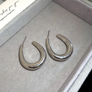 Close-up of silver U-shaped metal earrings on a grey velvet jewelry display tray