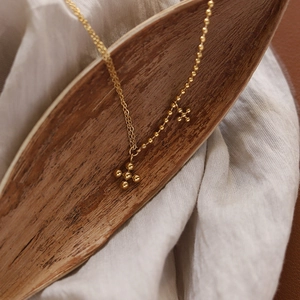 Detailed macro view of gold beaded chain necklace with cross pendants on wooden tray