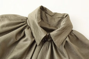 Macro detail of olive green bomber jacket featuring stand collar and pleated shoulder seams
