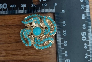 Detail of a hollow gold flower brooch with turquoise beads measured by a ruler