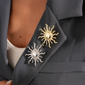 Detail of gold and silver sun-shaped brooches pinned on a dark grey blazer lapel