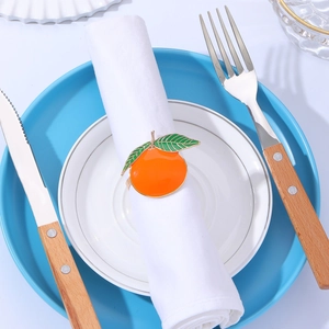 Close-up of orange napkin ring with green leaves on white linen and ceramic plates