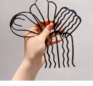Detail of hand holding a black metal wavy U-shaped hair pin for bun styling