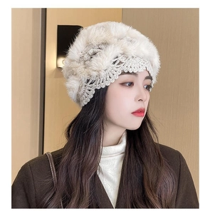 Detail of hand-crocheted cream beanie with fluffy fur ball pom-poms on the side