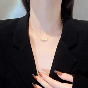 Close-up of a minimalist gold bead pendant necklace worn by a model in a black suit