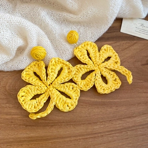 Detail of handcrafted yellow raffia woven flower earrings on a textured knit fabric