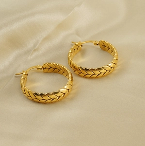 Détail de boucles d'oreilles dorées à texture tressée sur un fond en soie beige