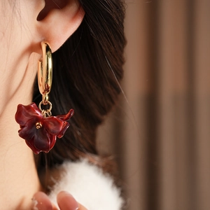 Detailed view of elegant C-shaped gold metal earrings with deep red floral resin petals