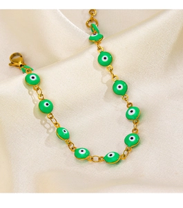 Detail of gold evil eye bracelet with green enamel beads on a cream silk fabric background