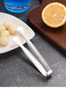 Macro shot of polished stainless steel sugar tongs on a table with lemon and blue drink