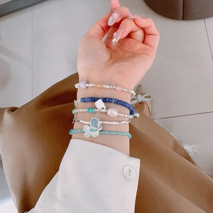 Close-up of stacked blue beaded bracelets with silver flower charms and white pearls