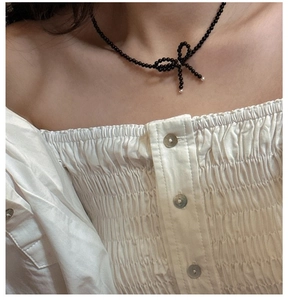 Elegant beaded necklace with black beads and a bow pendant worn by a model