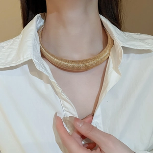 Detail of chunky gold choker necklace with textured ribbed finish worn by model