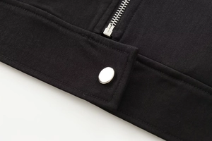 Detailed close-up of a black twill jacket featuring a silver zipper and metal snap button