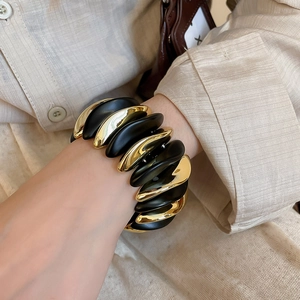 Detail of wide stretch bracelet with alternating gold metal and black matte wavy blocks