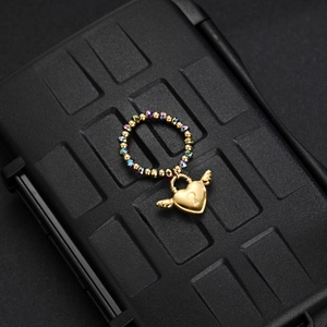 Detailed macro shot of beaded ring with golden winged heart lock pendant on textured base