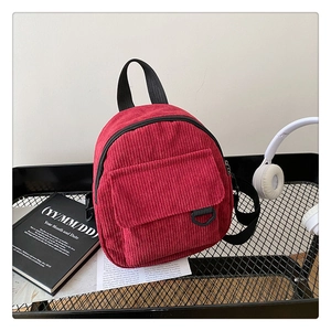Detail of red corduroy backpack showing ribbed fabric texture and metal D-ring on front pocket