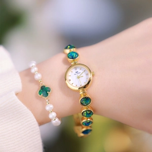 Close-up of gold jewelry watch featuring malachite inserts and white pearl clover bracelet