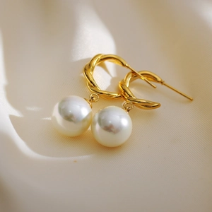 Exaggerated golden twisted hoop earrings with large teardrop pearls on silk background