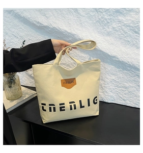 Close-up of cream canvas tote bag featuring brown leather logo patch and black lettering