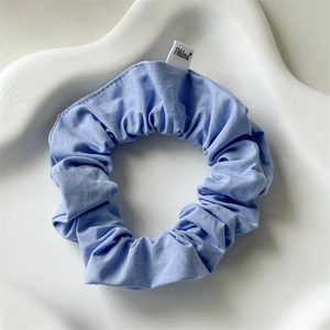 Detailed macro view of the blue cotton fabric texture and brand label on a soft scrunchie