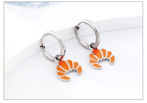 Macro detail of silver hoop earrings with orange enamel croissant charms on white background