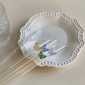 Pailles en verre transparent avec papillons colorés présentées dans un plat blanc