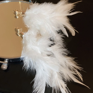 Detail of white feather tassel earrings with golden metal studs on black background