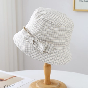 Détail d'un chapeau bob à carreaux beige avec un nœud sur un support en bois élégant