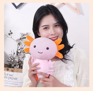 Pink axolotl plush toy with orange gills held by a smiling model in a cozy home setting